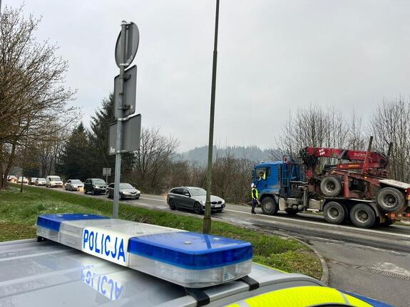 na pierwszym planie belka radiowozu, na planie drugim droga, stojące na niej pojazdy i policjant przeprowadzający badanie trzeźwości